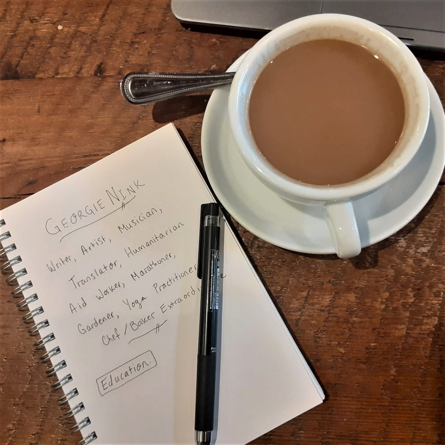 A mug of coffee on a wooden table next to a notepad outlining my name and byline at the top of my life resume.