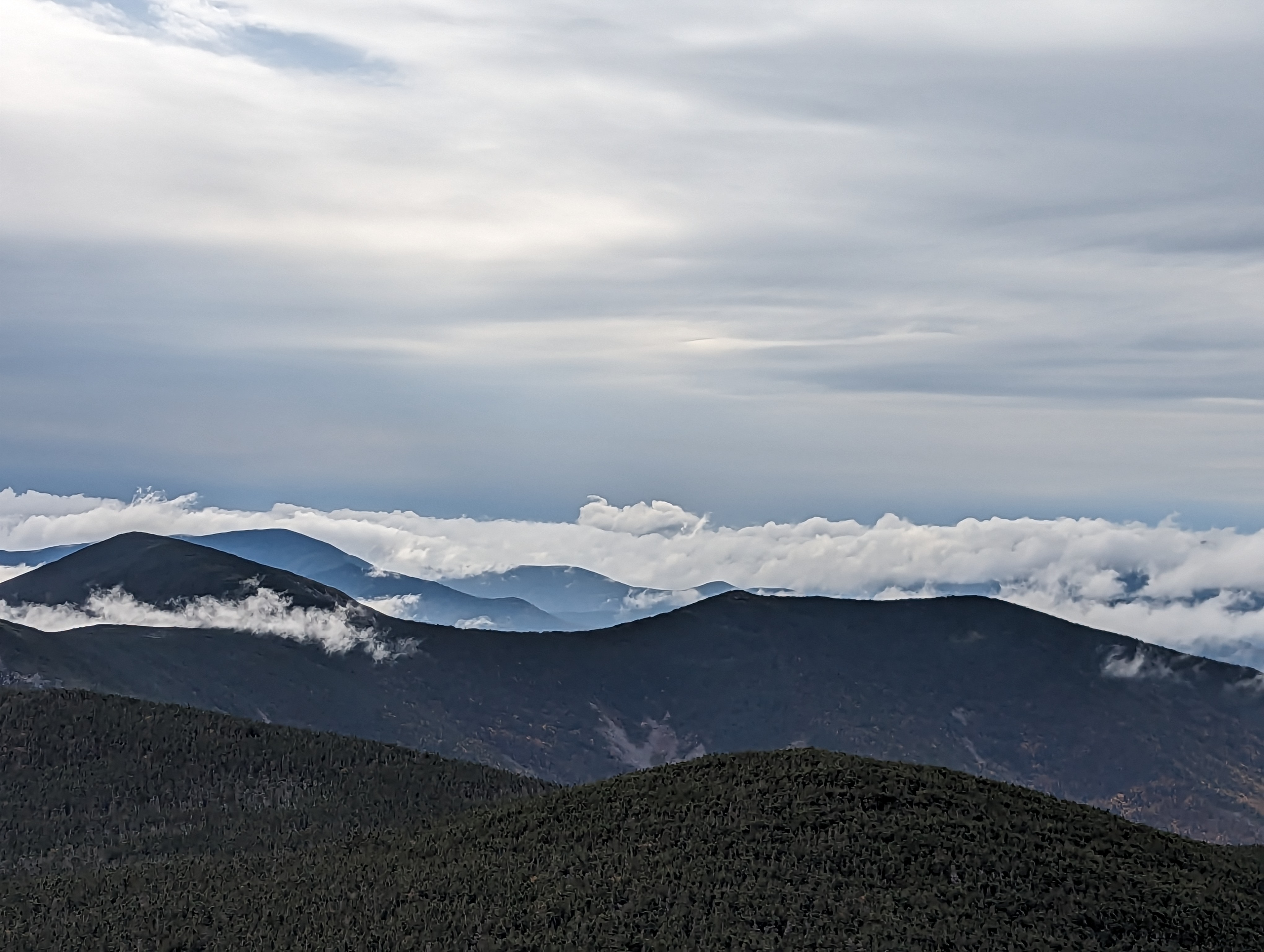 Clouds and mountain peaks interspersed in layers under a cloudy sky.
