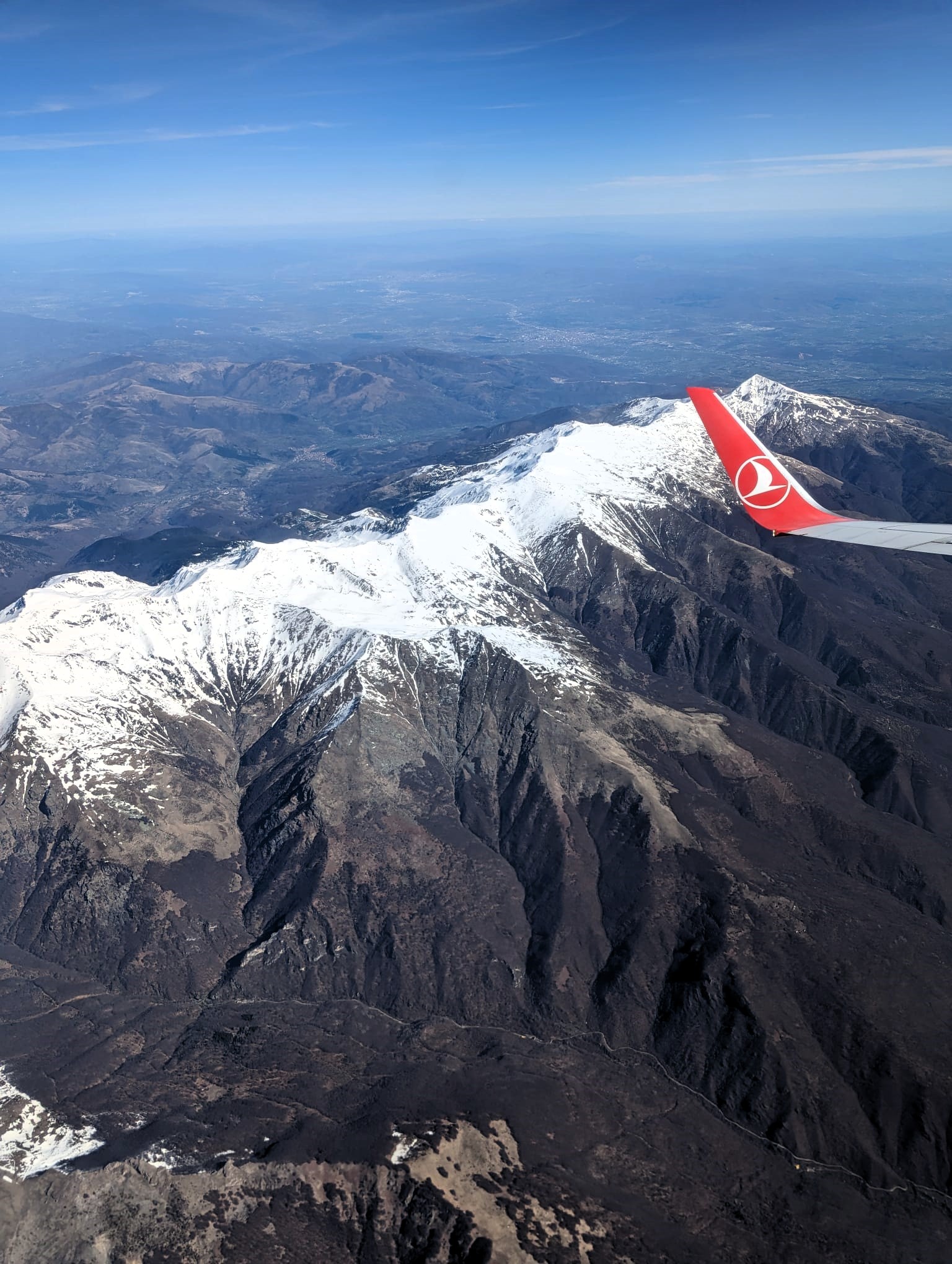Snow capped mountain peaks with the wing of an airplane flying over