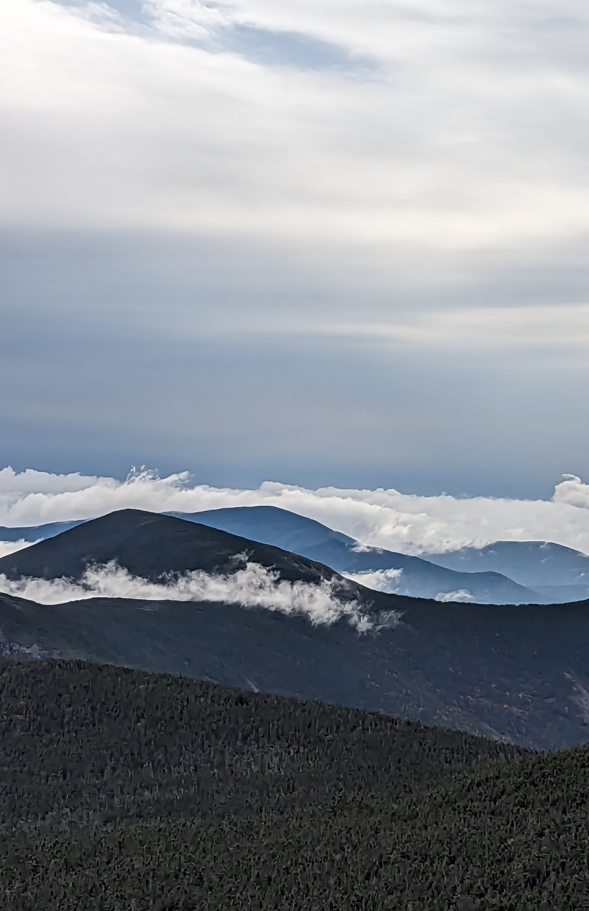 Dark mountains with clouds interspersed under a gray sky