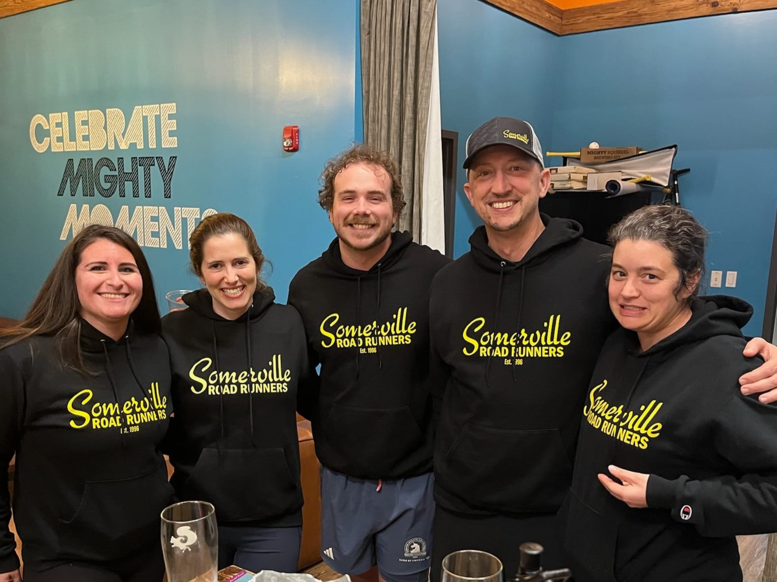 Five friends smiling and wearing the same black sweatshirt which reads Somerville Road Runners