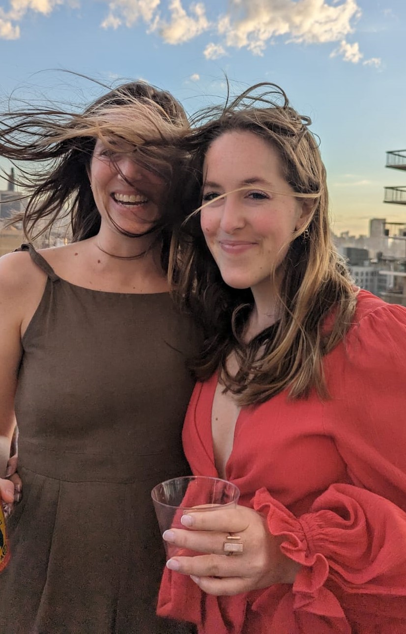 Two women smiling on a New York City rooftop with the wind blowing their hair around