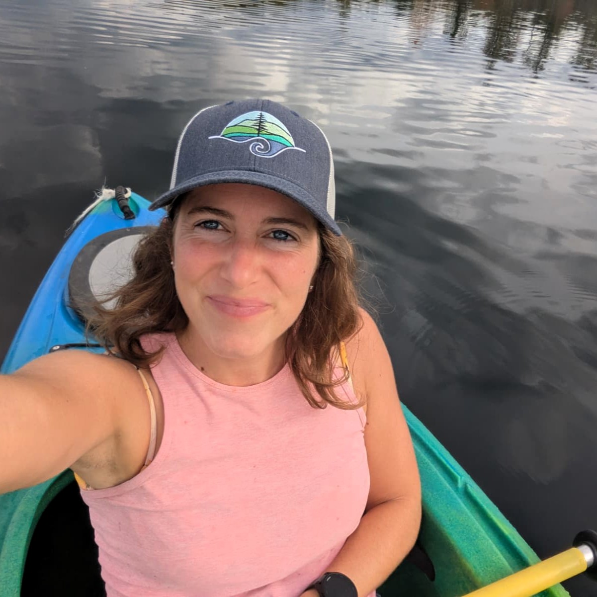 Woman wearing a pink shirt and blue baseball cap in a kayak against the background of a gray lake