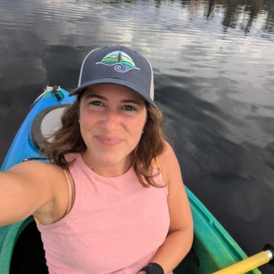Woman wearing a pink shirt and blue baseball cap in a kayak against the background of a gray lake